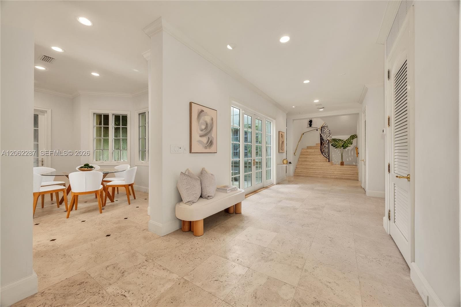 Open interior featuring large-format stone tile flooring, recessed lighting, double-paned glass French doors, and a staircase with a wrought-iron railing