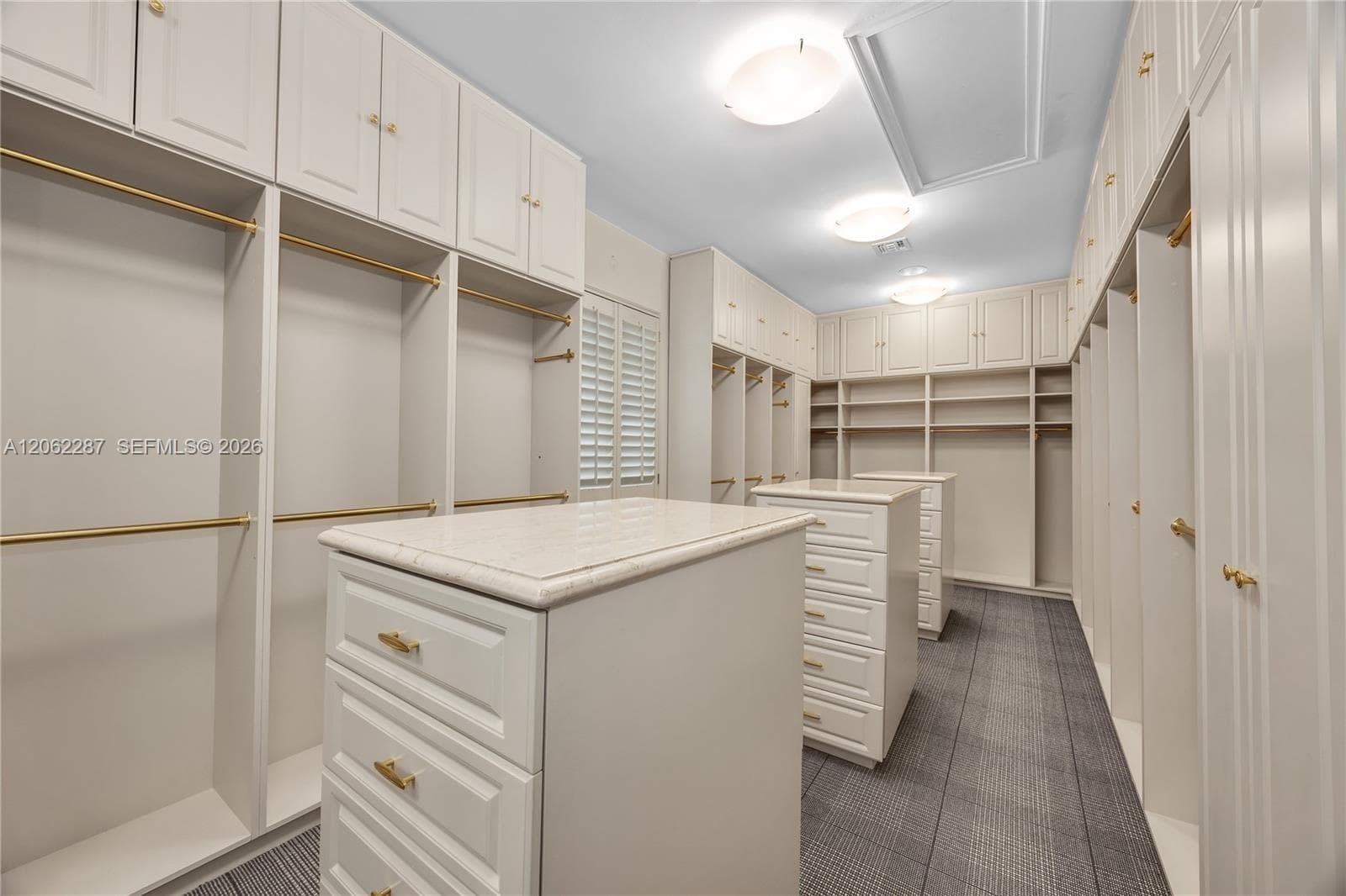 Custom built-in cabinetry featuring white shaker-style doors, dual islands with stone-composite countertops, matte gold hardware, tiered shelving, and hanging rods