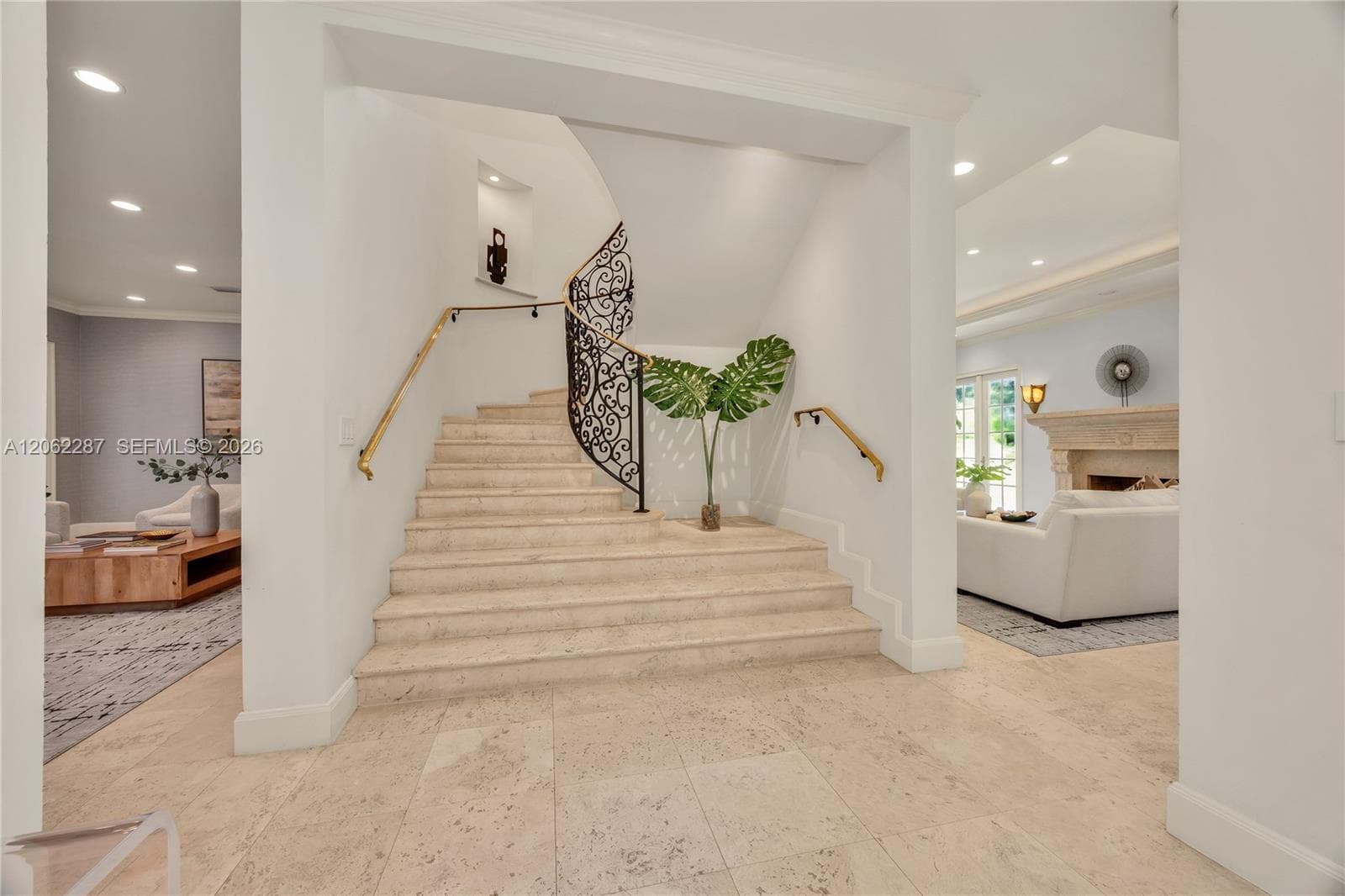 Grand foyer featuring a stone staircase with ornate iron railing, brass handrails, recessed wall niche, and natural stone flooring with recessed lighting