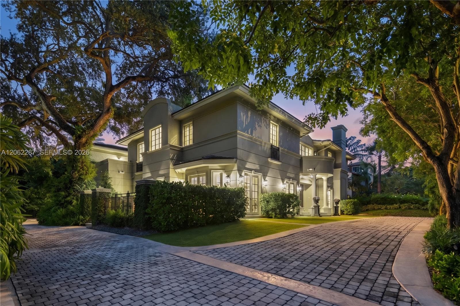 Two-story stucco exterior featuring architectural columns, multi-pane windows, arched entry, and a paver stone driveway
