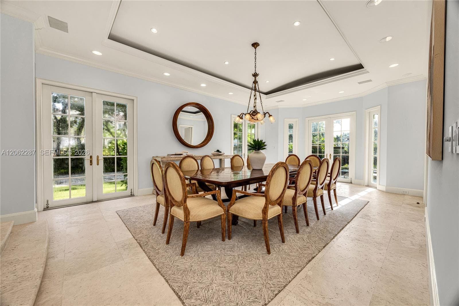Formal dining area featuring tray ceilings with recessed lighting, stone flooring, a multi-light chandelier, and dual sets of glass-paneled French doors