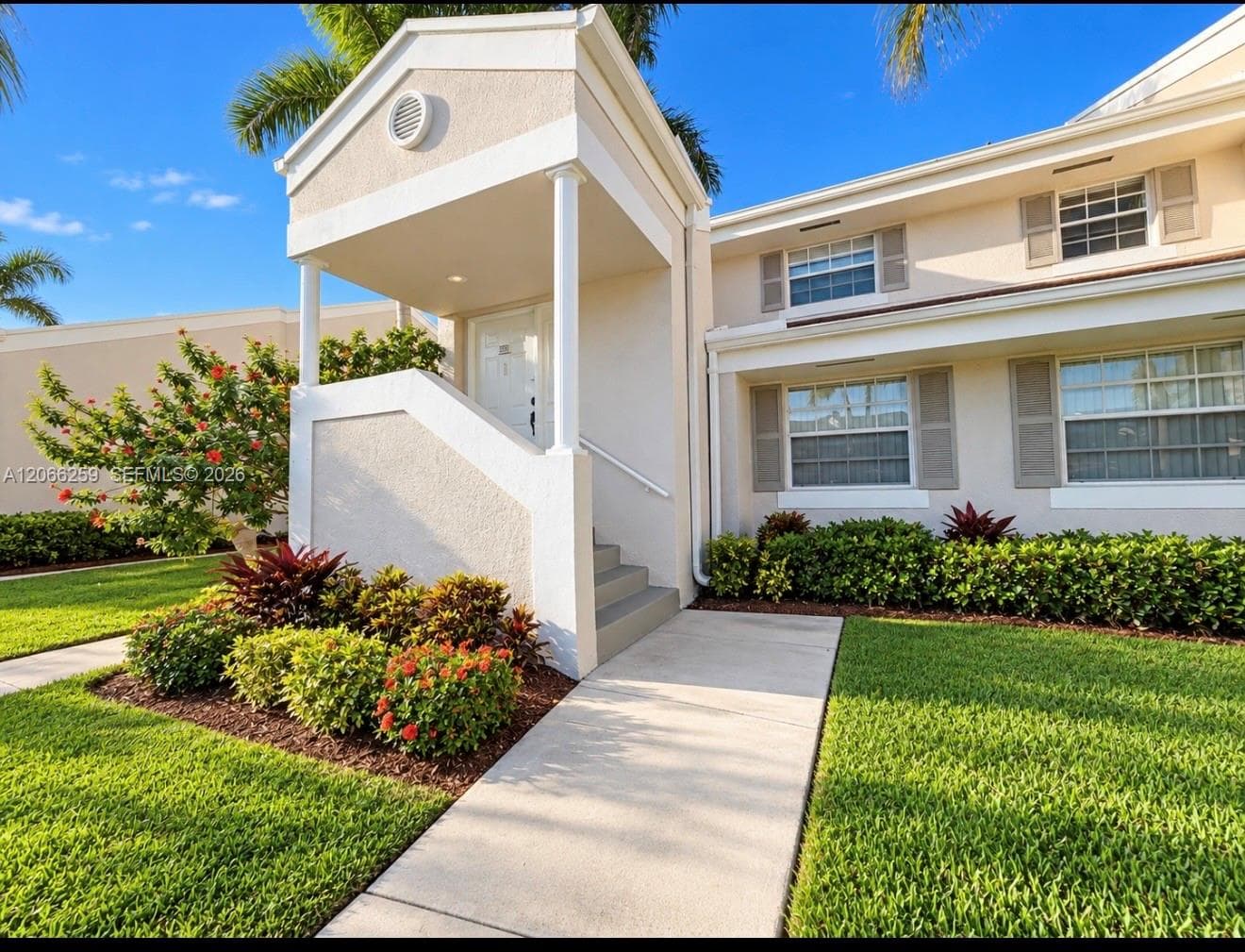 Stucco exterior featuring a covered entryway with column supports, concrete walkway, and landscaped garden beds