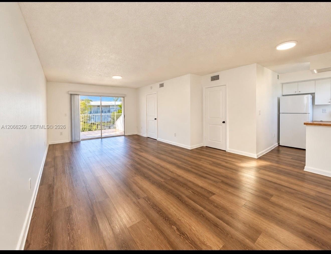 Open-concept floor plan featuring wood-finish flooring, sliding glass door access to a private balcony, and white cabinetry