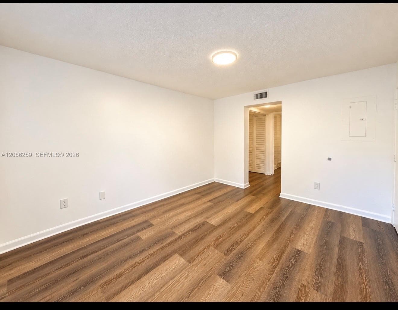 Interior space featuring wood-finish flooring, white walls, flush-mount lighting, and louvered closet doors