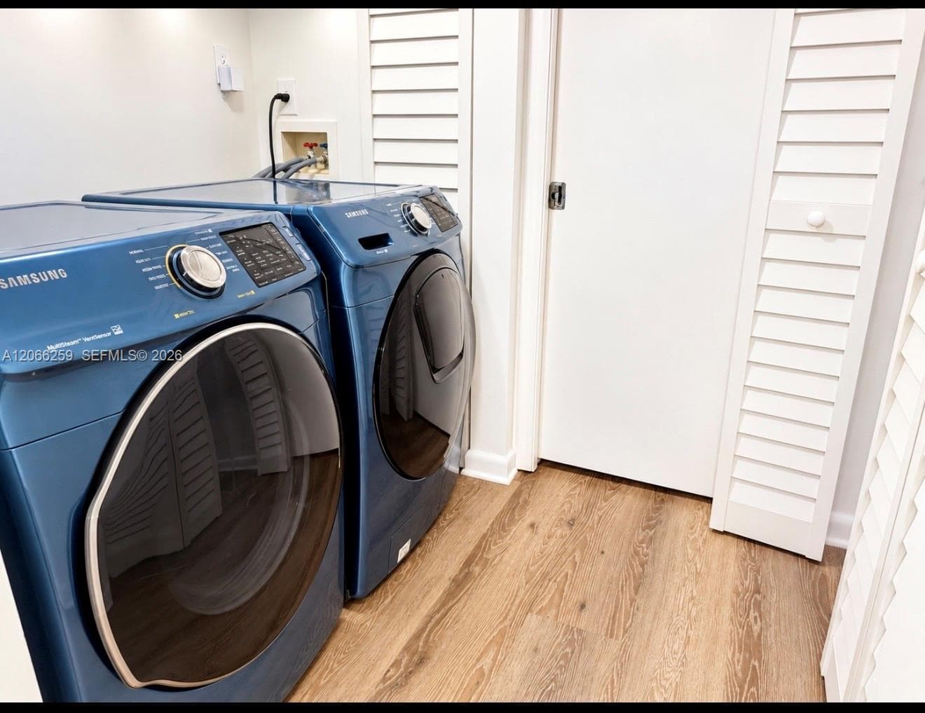 Laundry area featuring wood-finish flooring, white louvered bi-fold doors, and integrated appliance hookups