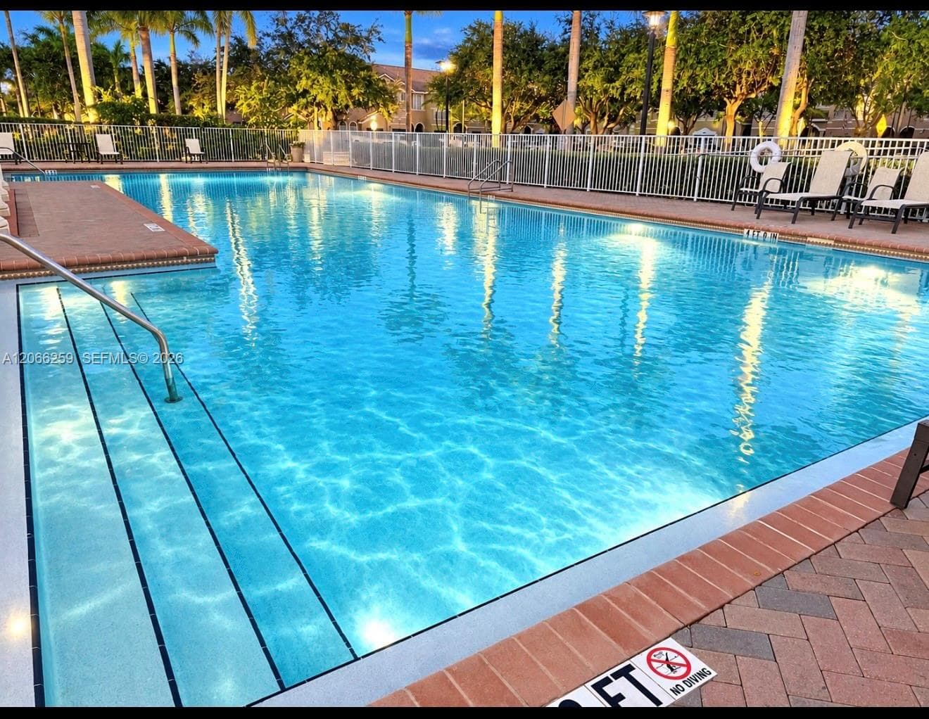 Swimming pool featuring built-in entry steps, stainless steel handrails, and a brick-paver deck border