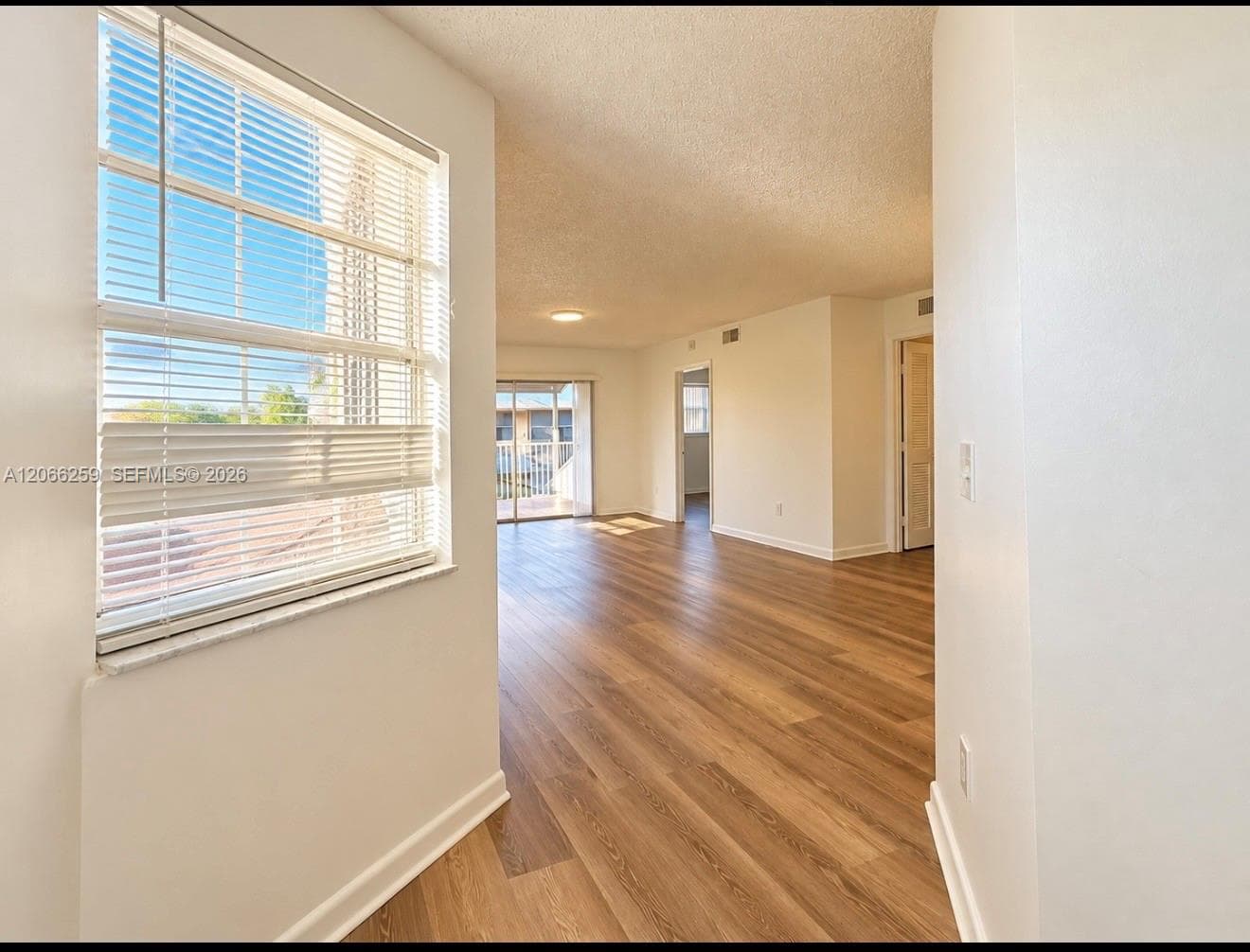 Open interior featuring wood-finish flooring, white walls, horizontal window blinds, and sliding glass doors
