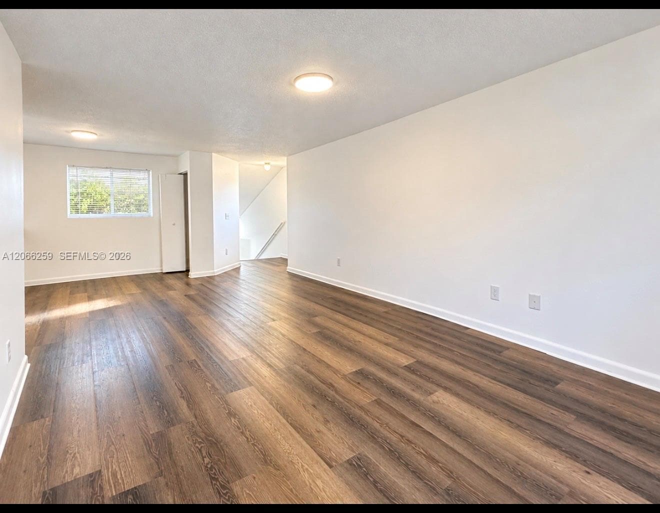 Open-concept interior featuring wood-finish flooring, neutral wall tones, dual flush-mount ceiling lights, and a single-pane window
