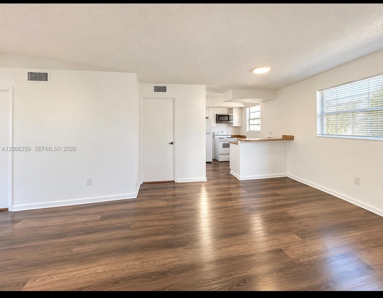 Neutral-toned interior featuring wood-finish flooring, a breakfast bar, and white cabinetry
