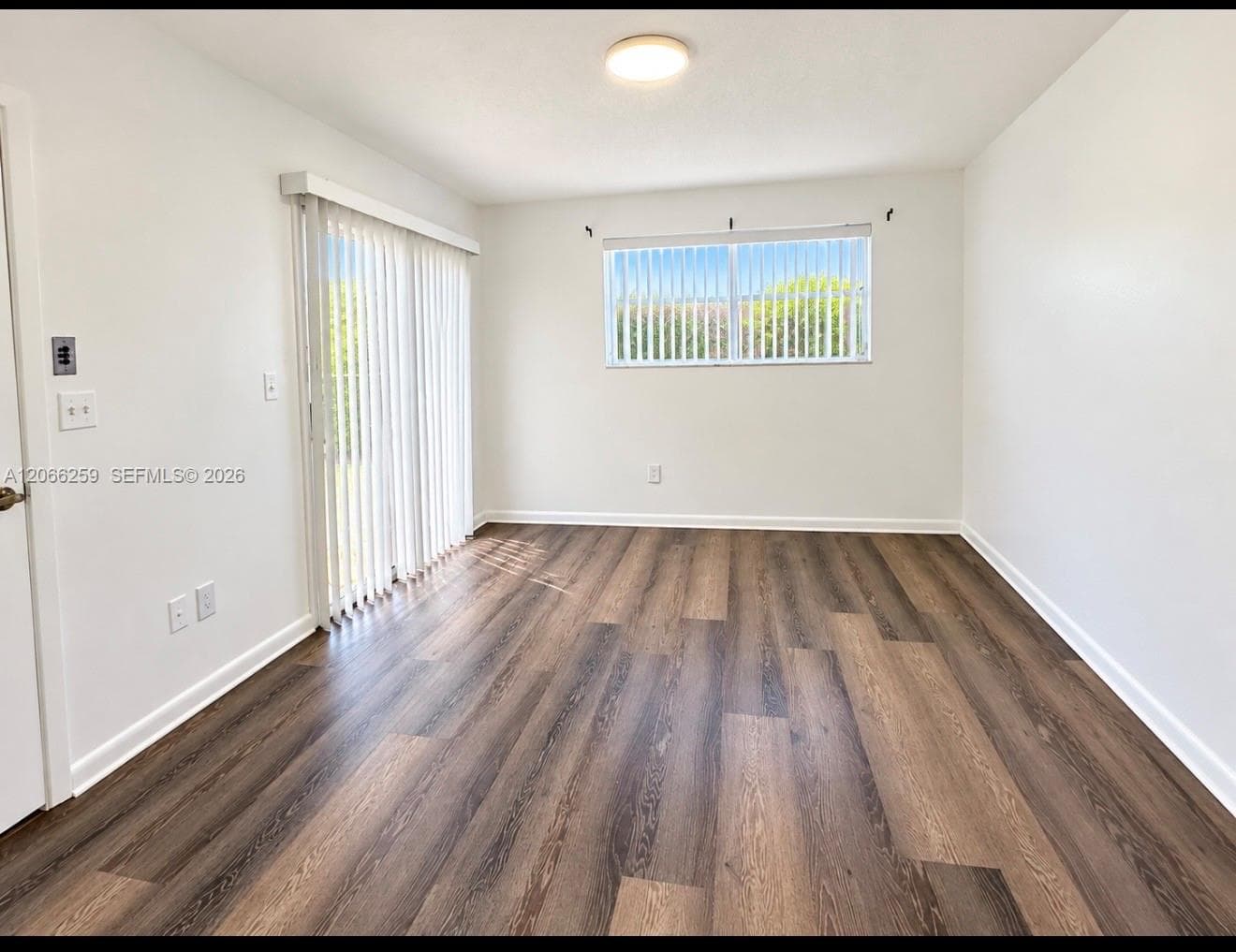 Interior space featuring wood-finish flooring, sliding glass patio door with vertical blinds, single horizontal window, and flush-mount ceiling lighting