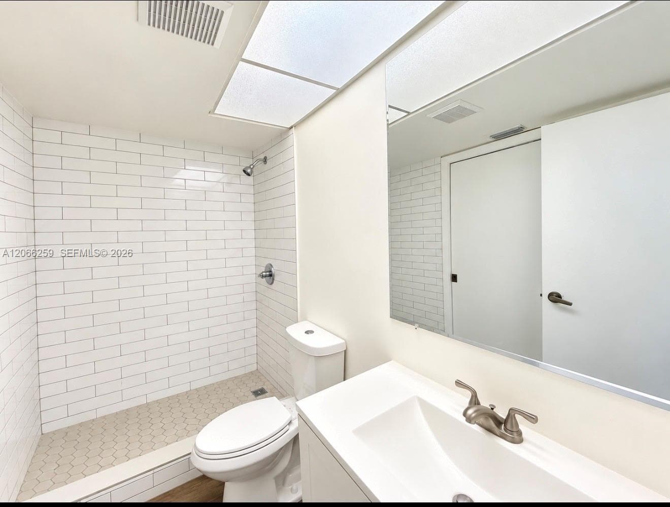 Bathroom featuring a walk-in shower with white subway tile walls and hexagonal floor tiling, a vanity with an integrated basin, a large wall-mounted mirror, and recessed lighting