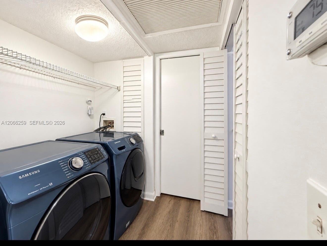 Laundry space featuring wood-finish flooring, white louvered closet doors, and wall-mounted wire shelving