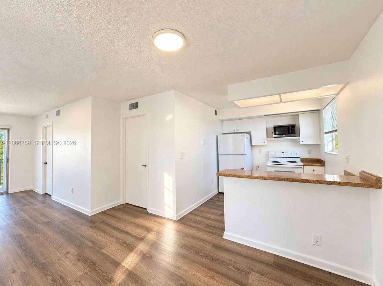 Kitchen featuring wood-finish flooring, a stone-surfaced breakfast bar, white cabinetry, and built-in appliances