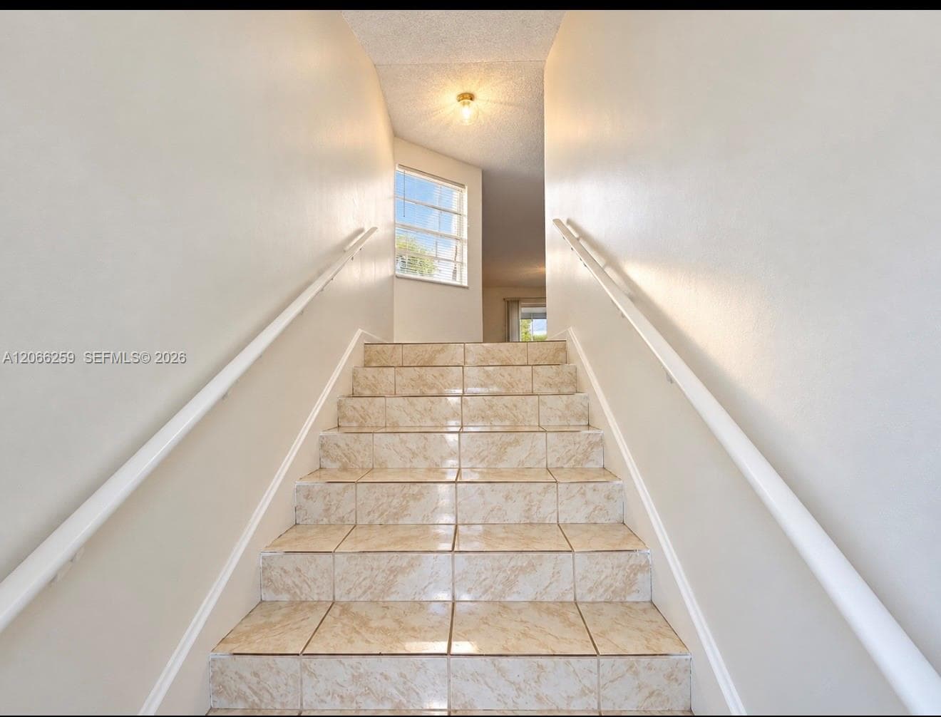 Staircase featuring tiled treads, dual white handrails, and a multi-pane window