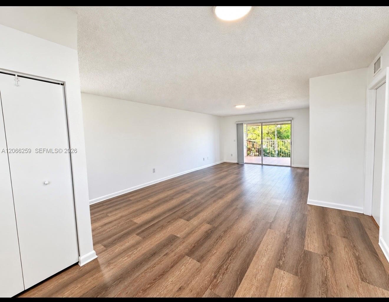 Open-concept interior featuring wood-finish flooring, sliding glass door, and built-in closet storage