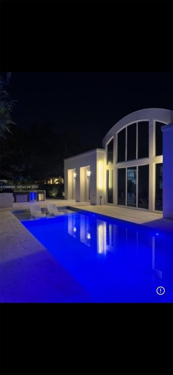 Swimming pool with integrated sun shelf and stone pool deck, featuring a building exterior with arched windows and recessed wall lighting
