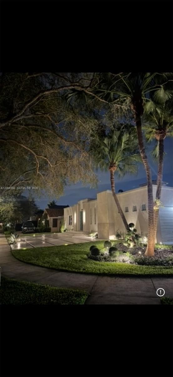 Stucco exterior featuring a paved driveway, manicured landscaping, mature palm trees, and integrated landscape lighting