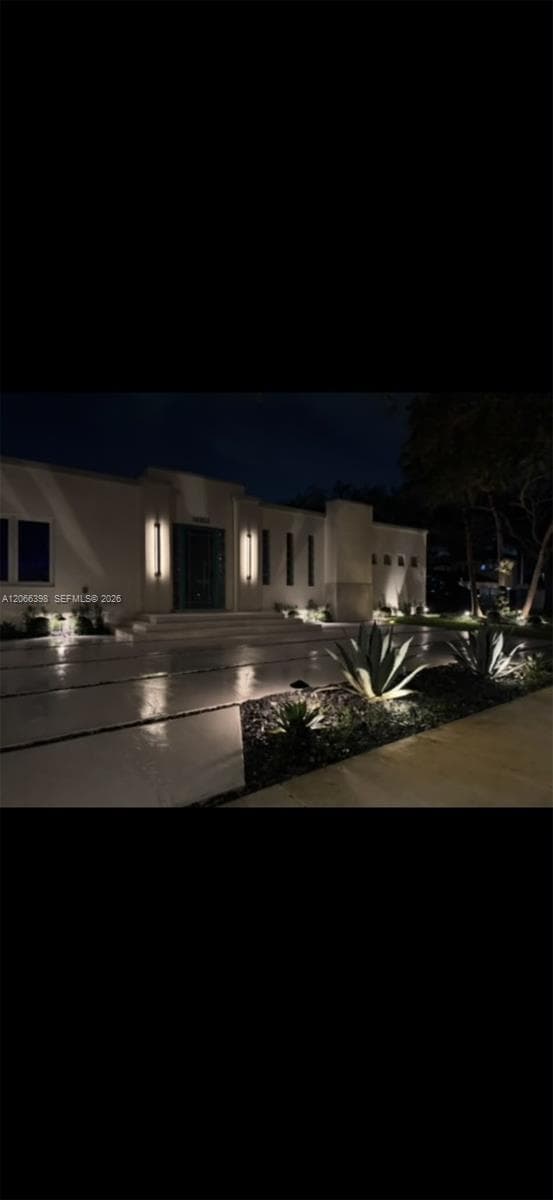 Contemporary exterior featuring smooth stucco finish, structured landscape beds, linear concrete driveway, and vertical wall-mounted lighting