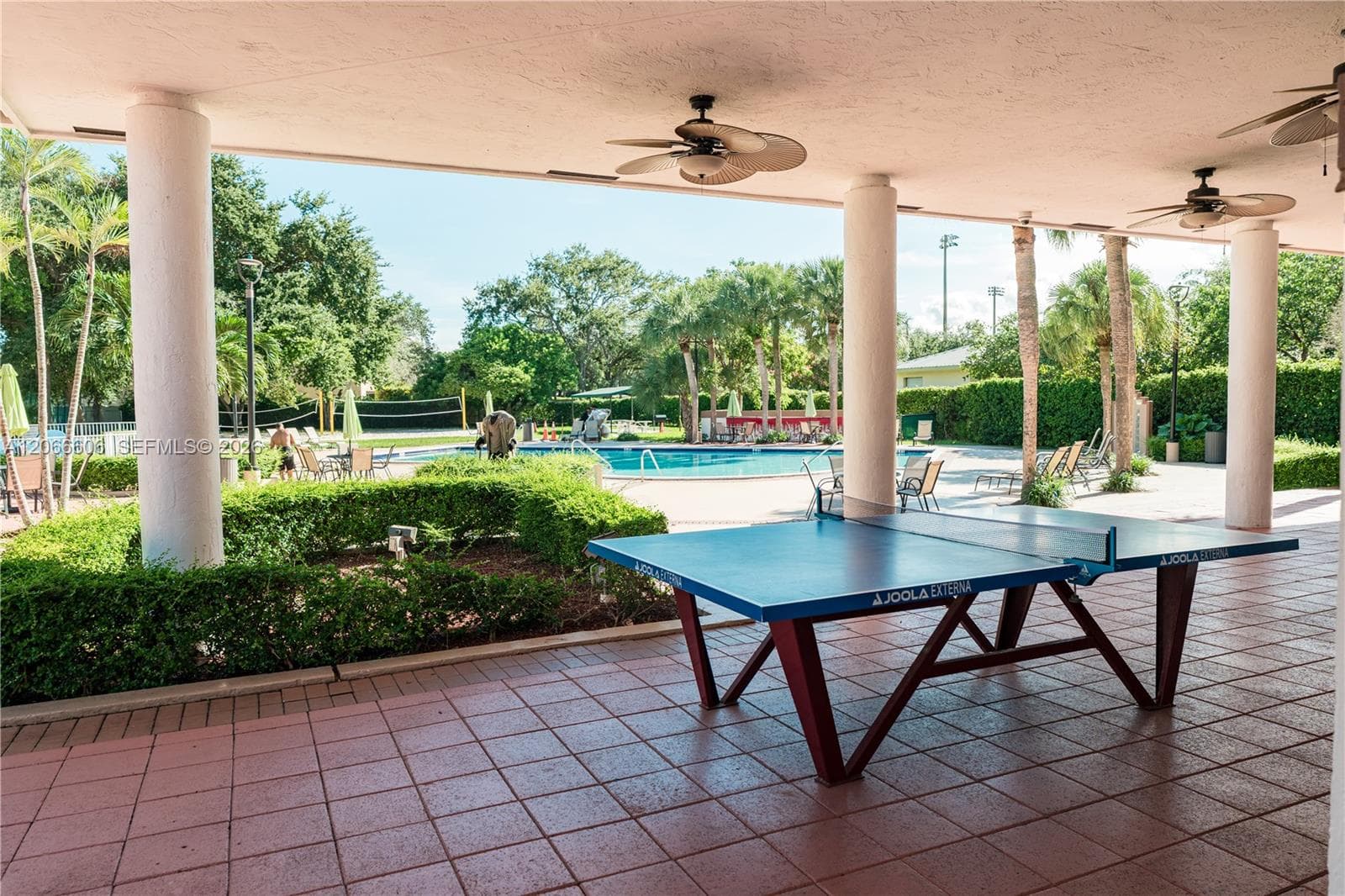 Covered patio with ceramic tile flooring, structural columns, and ceiling fans, overlooking an outdoor swimming pool and landscaped grounds