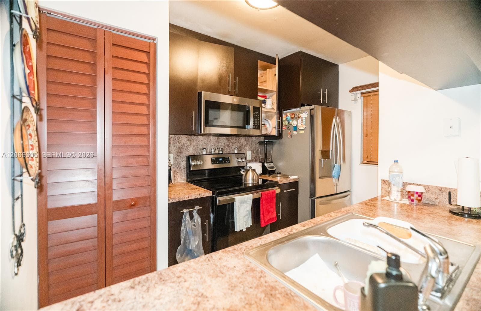 Kitchen featuring dark wood cabinetry, stainless steel appliances, solid surface countertops, and louvered closet doors