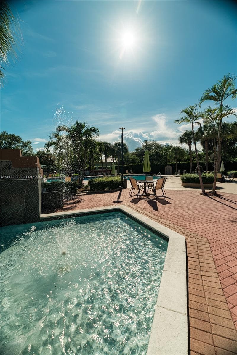 Swimming pool featuring a stone fountain, surrounded by brick paver decking and mature palm trees