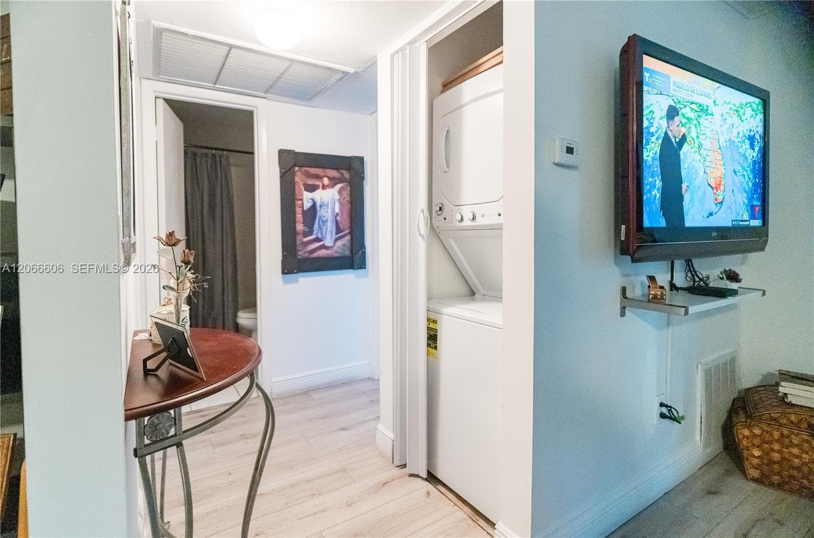 Laundry area featuring a stacked washer and dryer unit enclosed by bi-fold doors, wood-finish flooring, and a wall-mounted metal shelving bracket