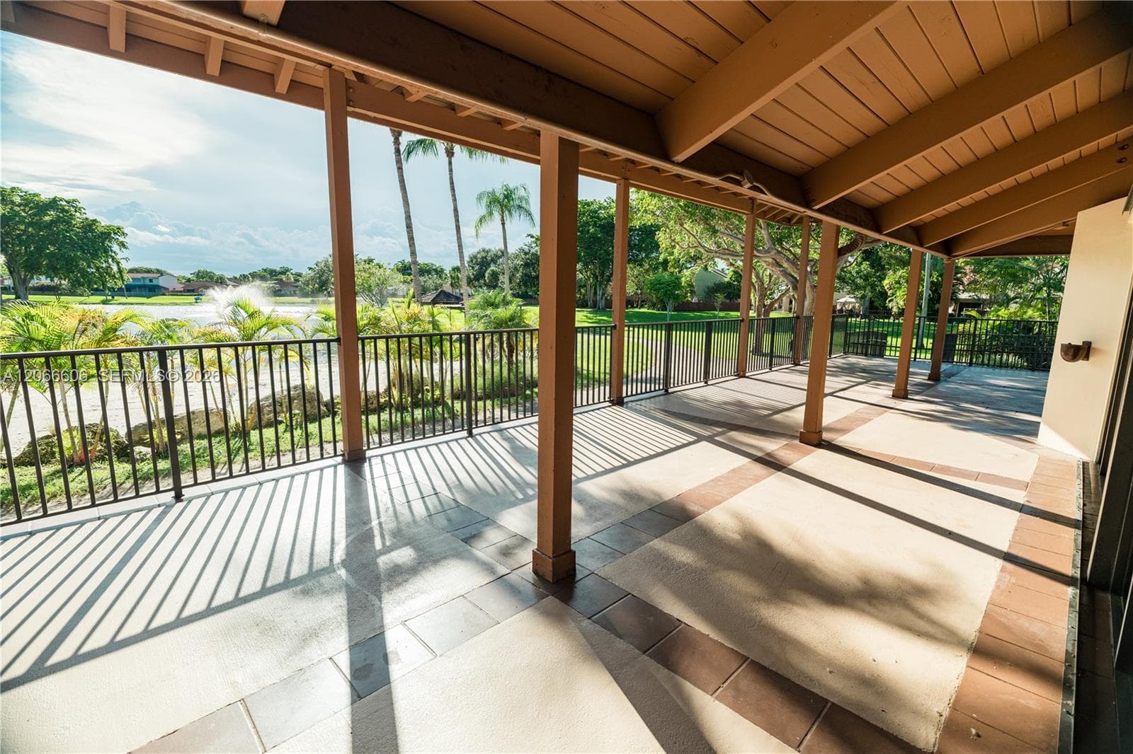 Covered patio featuring a wood-beam ceiling, decorative tile flooring, and metal railings overlooking a landscaped outdoor space