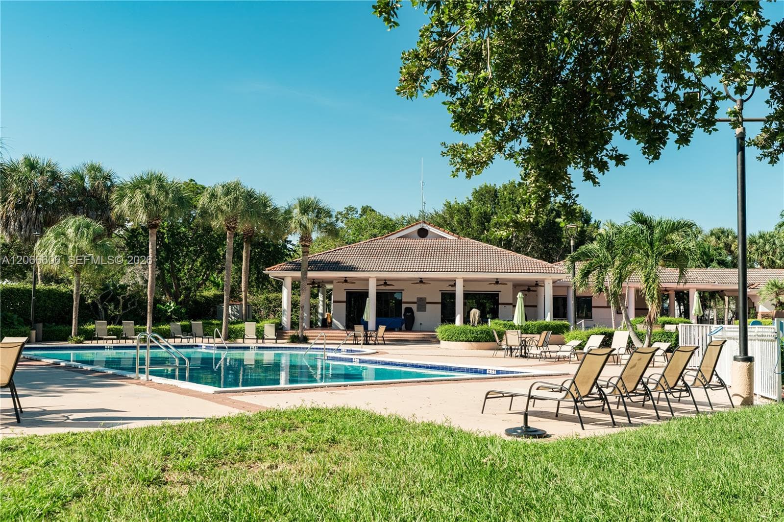Community pool featuring a concrete deck, built-in structural columns, tile-roof clubhouse, and surrounding mature landscaping