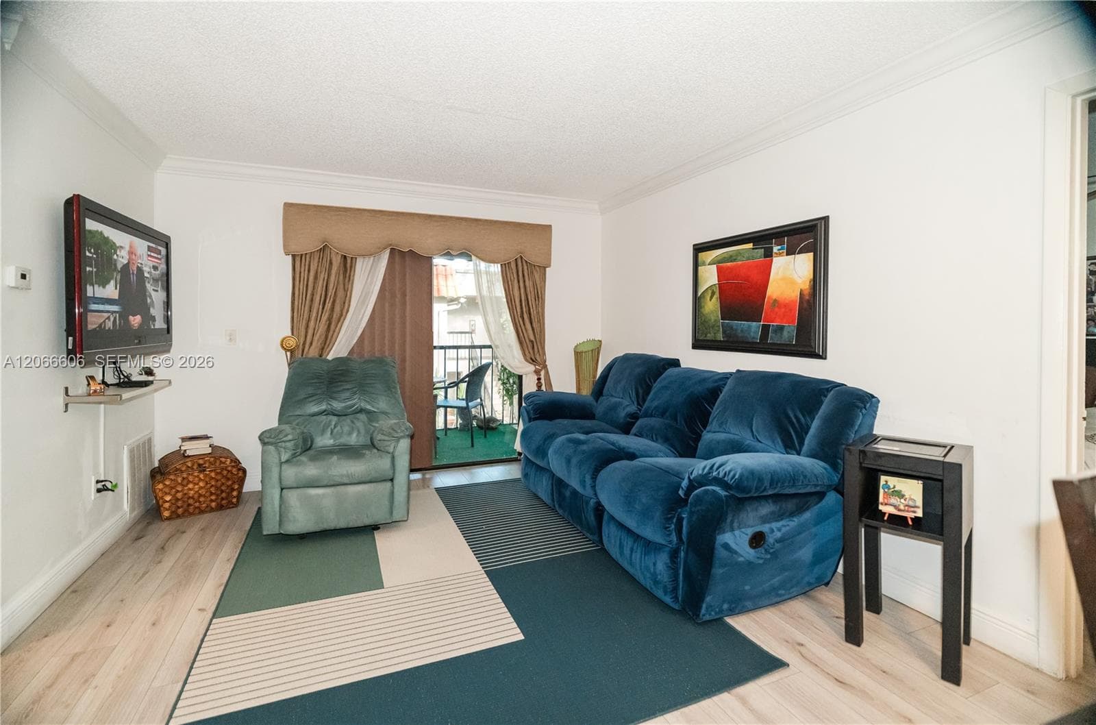 Living area featuring wood-finish flooring, crown molding, and a sliding glass door providing access to a balcony