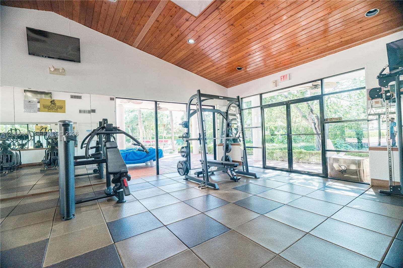Vaulted wood-plank ceiling, floor-to-ceiling glass panel walls, mirrored wall, and large-format tile flooring