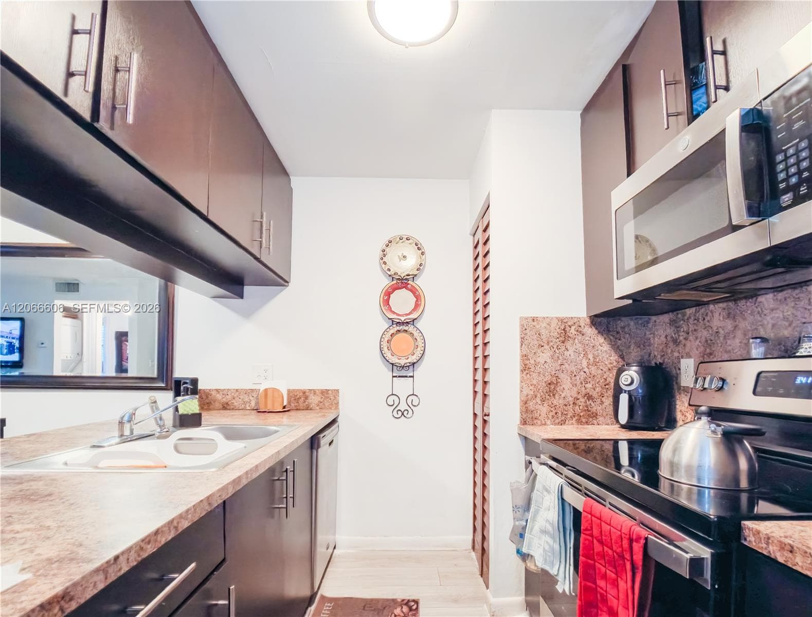 Galley-style kitchen featuring dark-toned cabinetry, laminate countertops, a stainless steel built-in microwave, and wood-finish flooring