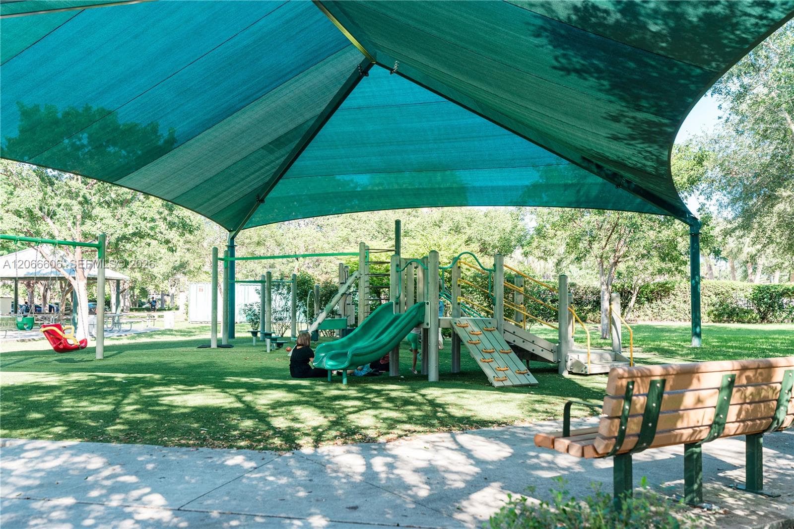 Recreational area featuring a large overhead sun shade, climbing structures, multiple slides, and integrated bench seating