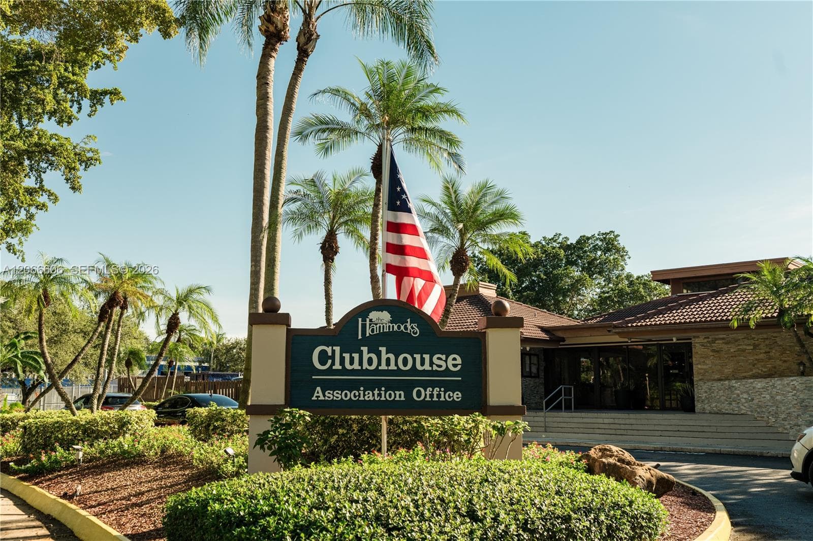 Clubhouse facility featuring stone-veneer exterior accents, a tiled roof, and landscaped grounds with mature palm trees