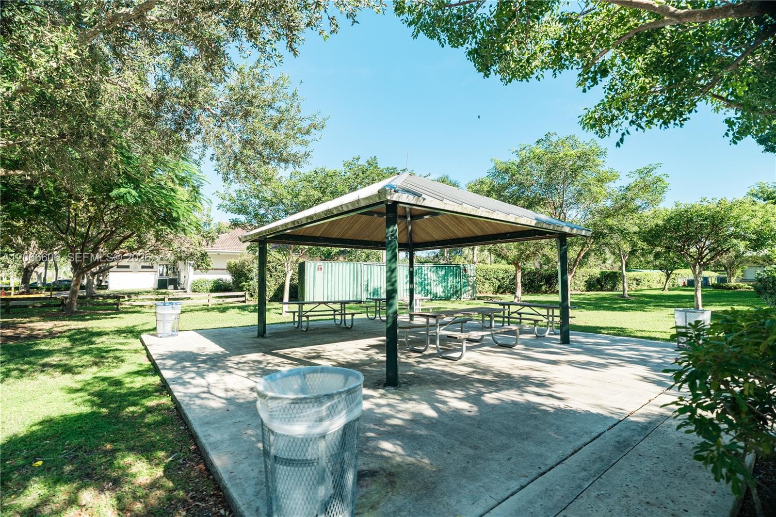 Outdoor pavilion featuring a metal-roofed structure, concrete pad, and mature shade trees