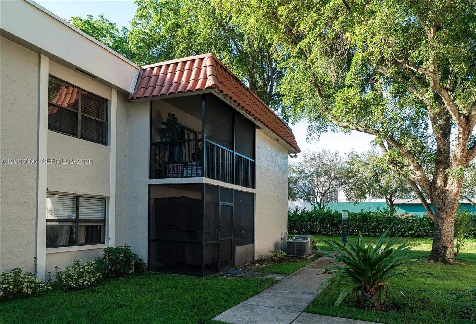 Two-story stucco exterior featuring a tiled hip roof, dual stacked screened-in lanais with metal railings, and a concrete walkway
