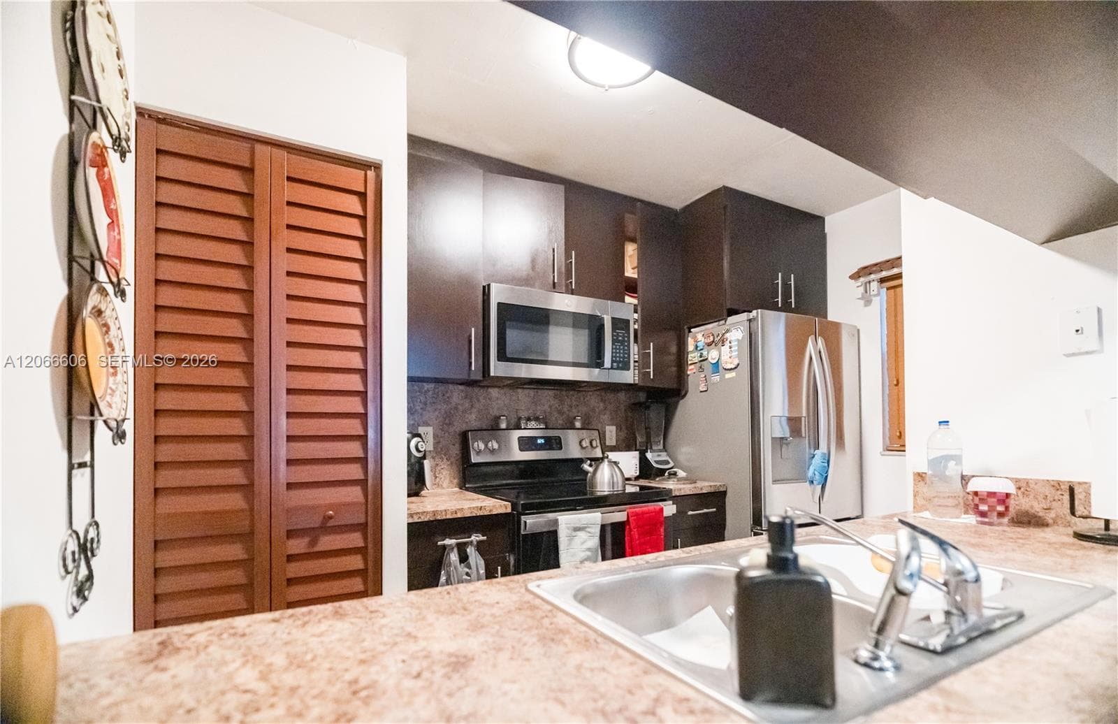 Kitchen featuring dark wood-finish cabinetry, stainless steel appliances, speckled stone-finish countertops, and dual-basin stainless steel sink with a high-arch faucet