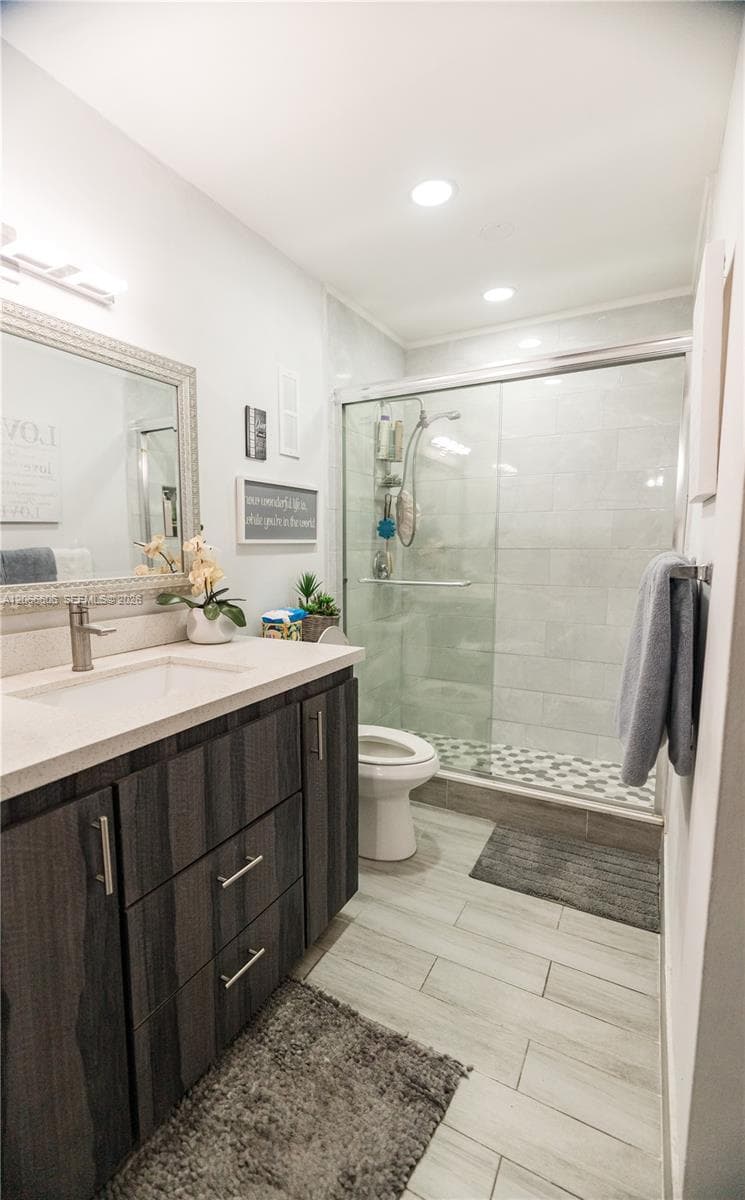 Modern vanity featuring a stone-composite countertop, rectangular undermount sink, and dark wood-grain cabinetry, complemented by tile flooring, recessed lighting, and a glass-enclosed shower with tiled surround