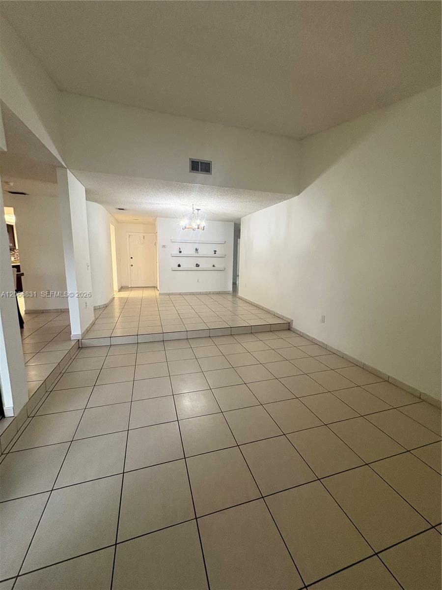 Open-concept interior featuring light-toned tile flooring, a multi-level split-floor design, recessed wall shelving, and a decorative ceiling-mounted chandelier