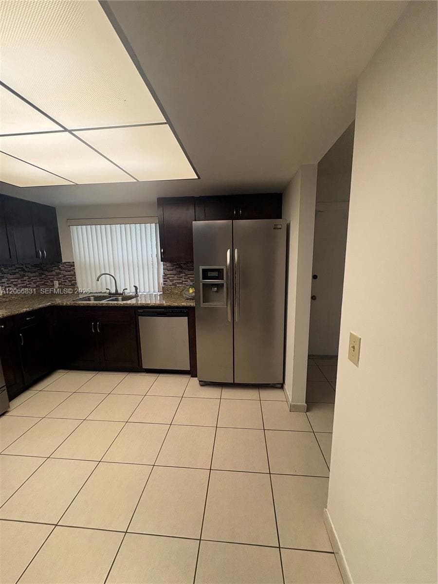 Kitchen featuring dark wood cabinetry, stone countertops, stainless steel appliances, a mosaic tile backsplash, and tile flooring