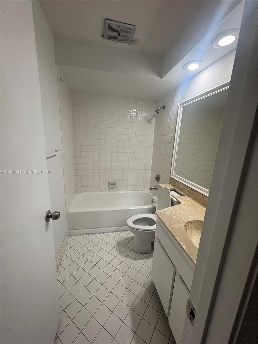 Bathroom featuring a vanity with a solid-surface countertop, integrated basin, full-width mirror, tile-surround bathtub, and diagonal-pattern floor tiling
