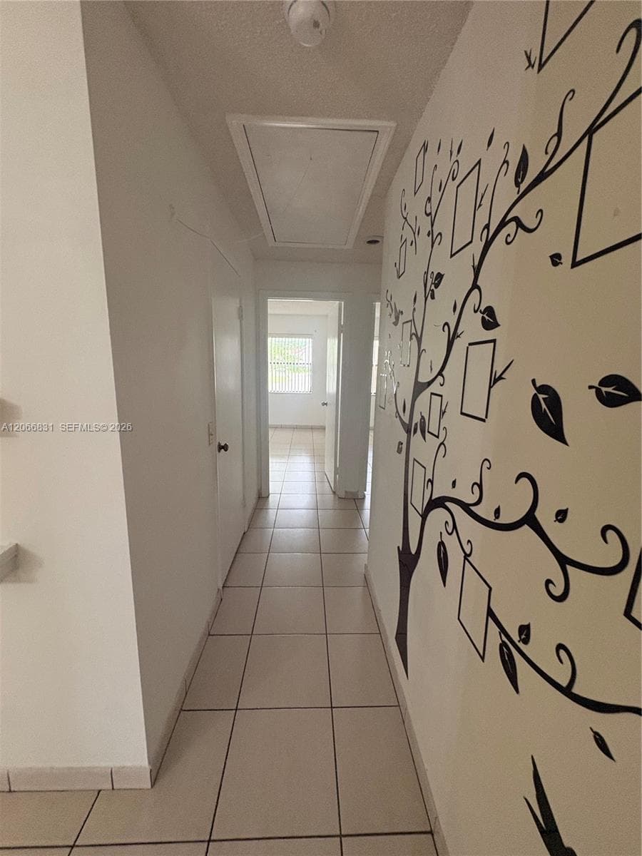 Interior hallway featuring neutral ceramic tile flooring and white doors with metallic hardware