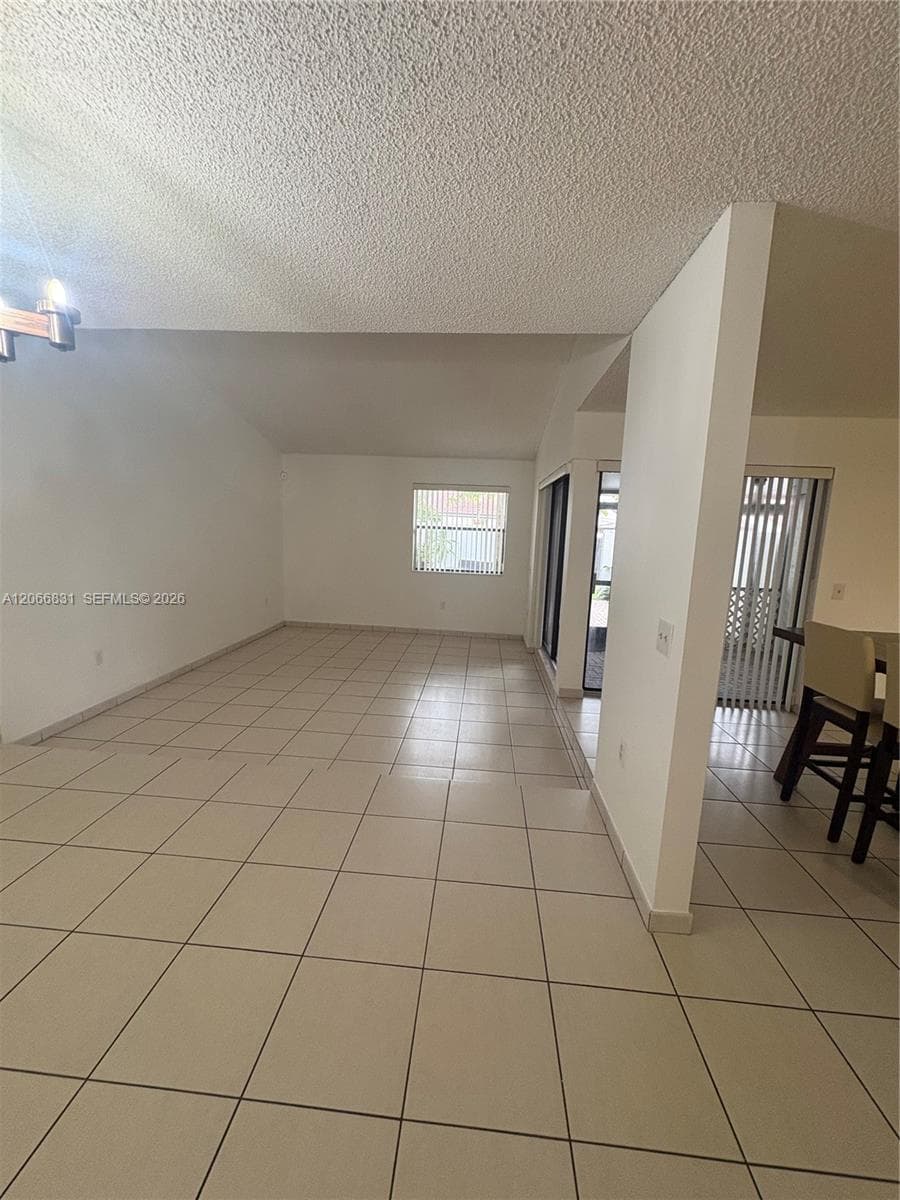 Open-concept interior featuring neutral tile flooring, vaulted ceilings, and sliding glass doors with vertical blinds