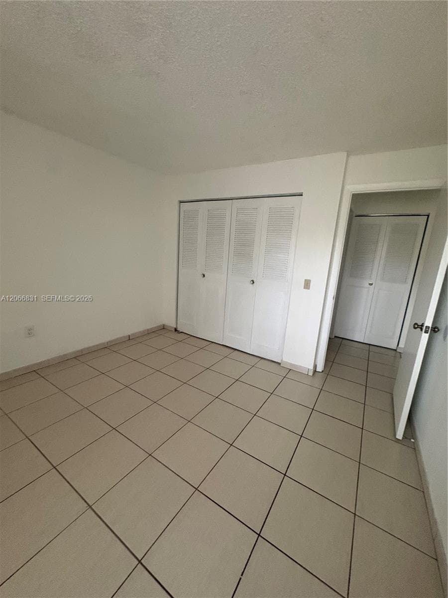 Neutral-toned tile flooring, white walls, and built-in closet storage with louvered doors