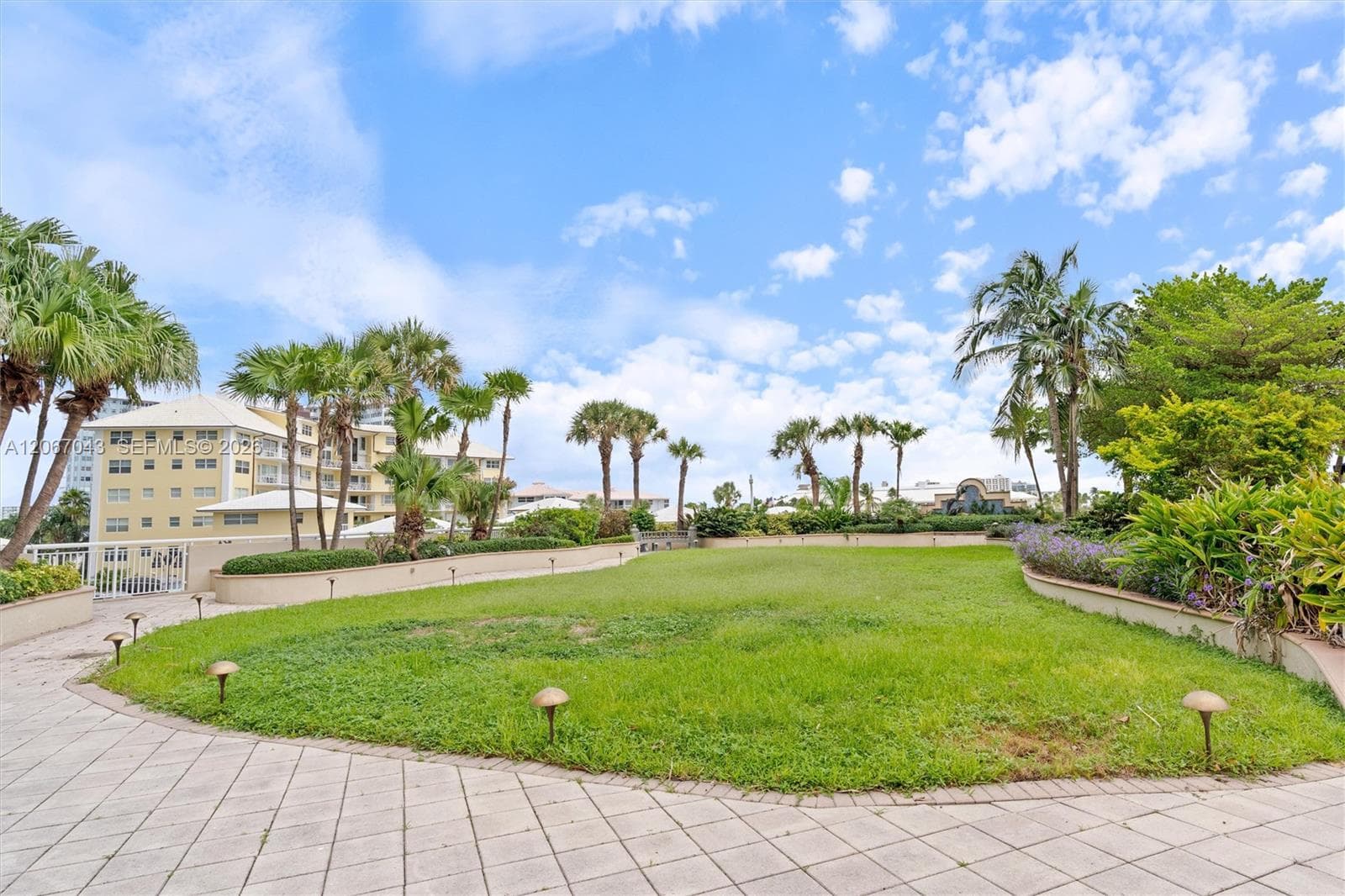 Expansive lawn featuring perimeter landscaping, palm trees, stone-paved pathways, and integrated low-voltage lighting