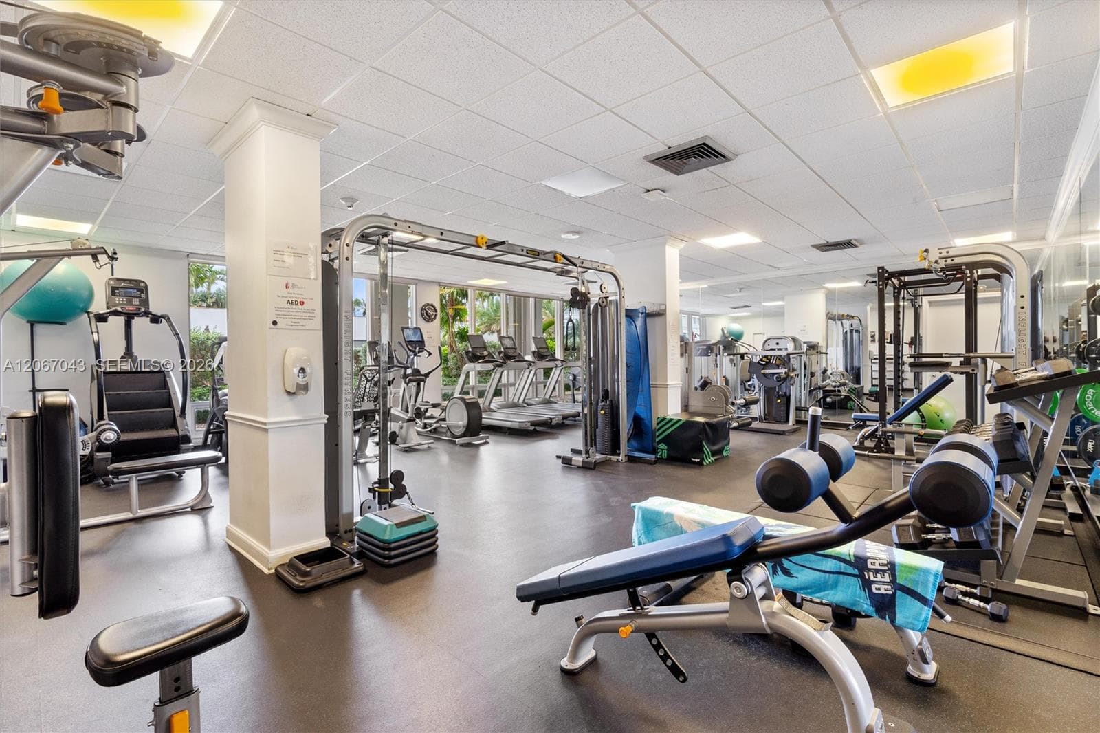 Fitness center featuring a rubberized floor, recessed ceiling lighting, structural columns, and wall-to-wall mirrors