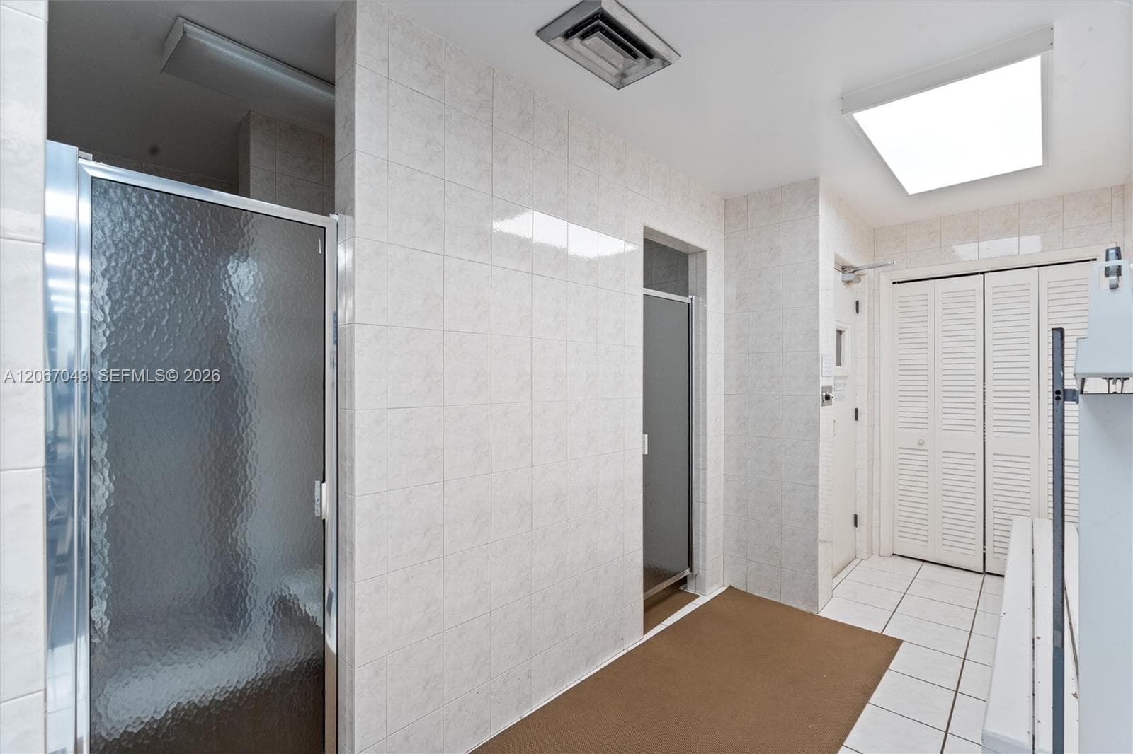 Walk-in shower with a glass pivot door, ceramic wall tile, recessed lighting, and louvered closet doors