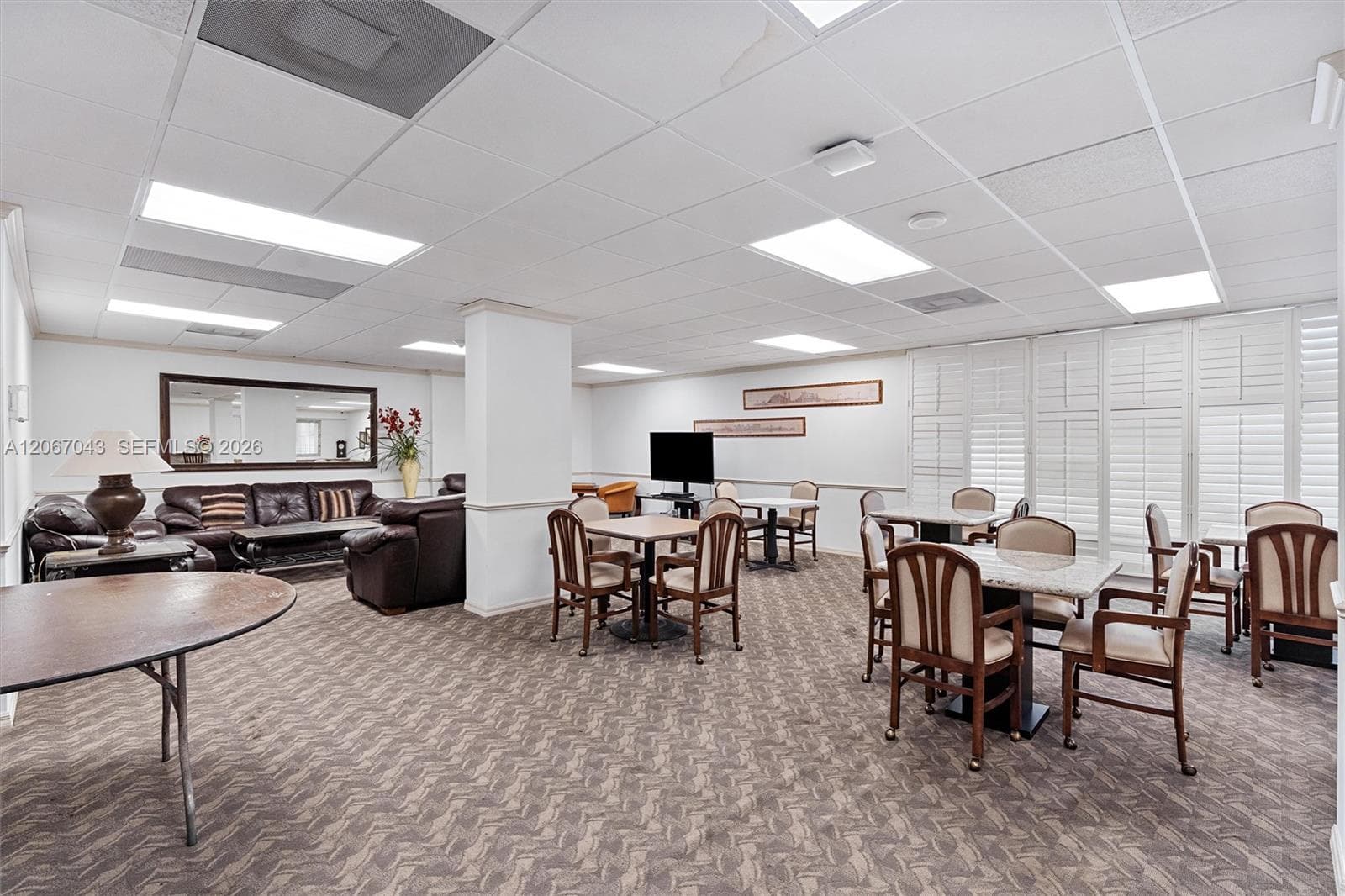 Open-concept space featuring recessed grid ceiling lighting, patterned wall-to-wall carpeting, and white window shutters