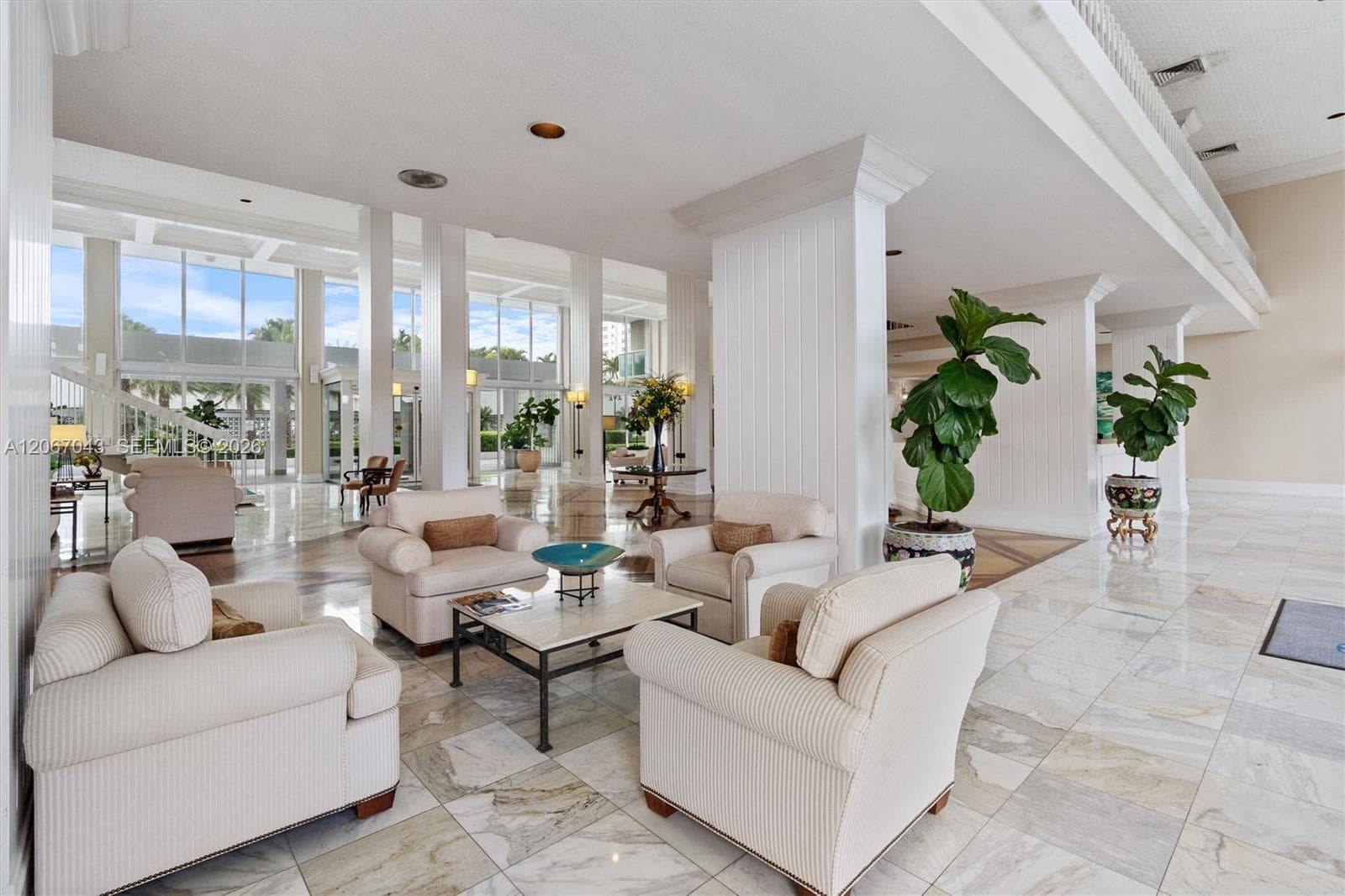 Open-concept lobby featuring polished stone tile flooring, floor-to-ceiling glass paneling, structural columns, and recessed lighting