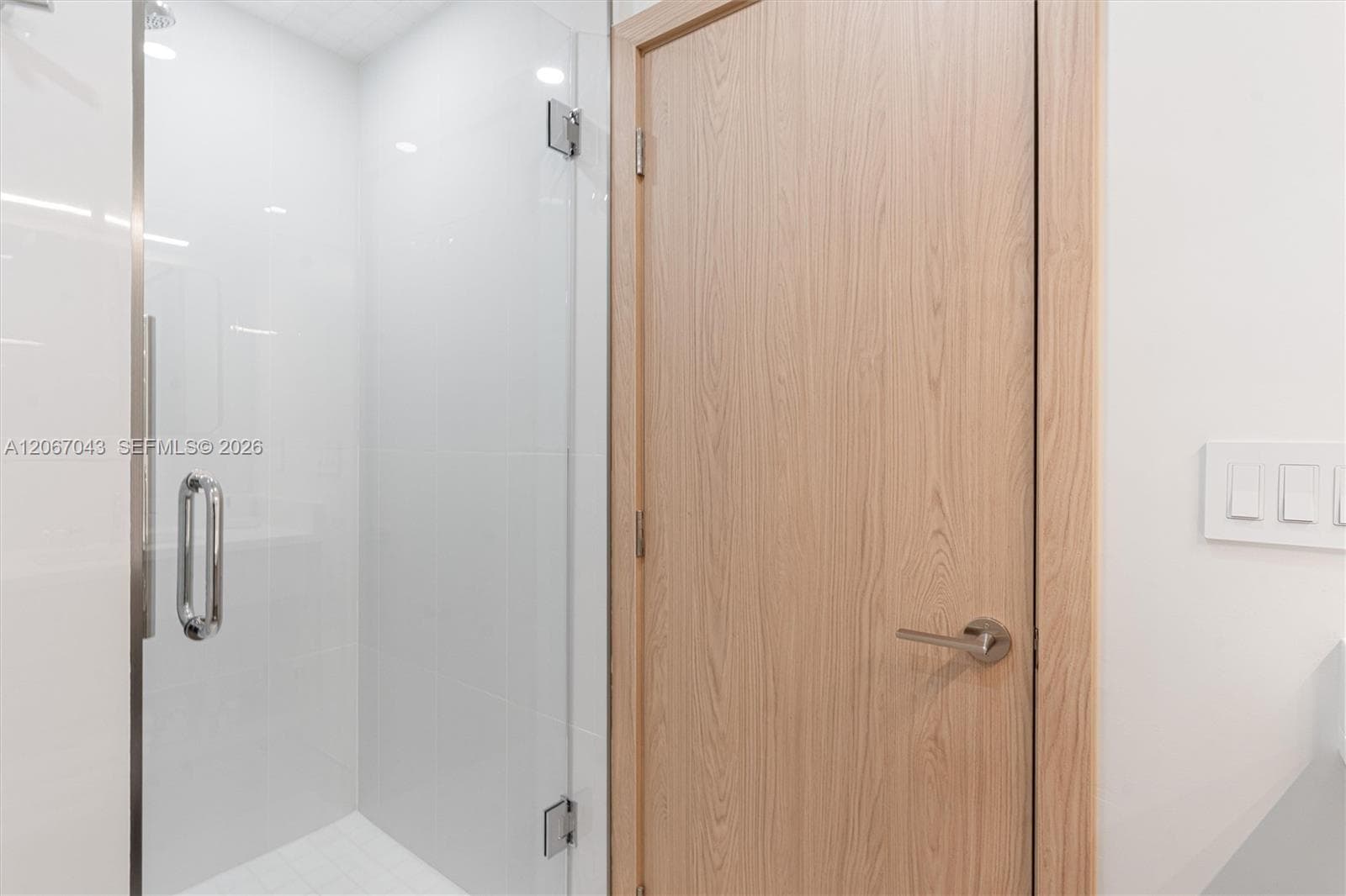 Frameless glass shower enclosure with polished chrome hardware, paired with a solid wood-finish interior door featuring a brushed nickel lever handle