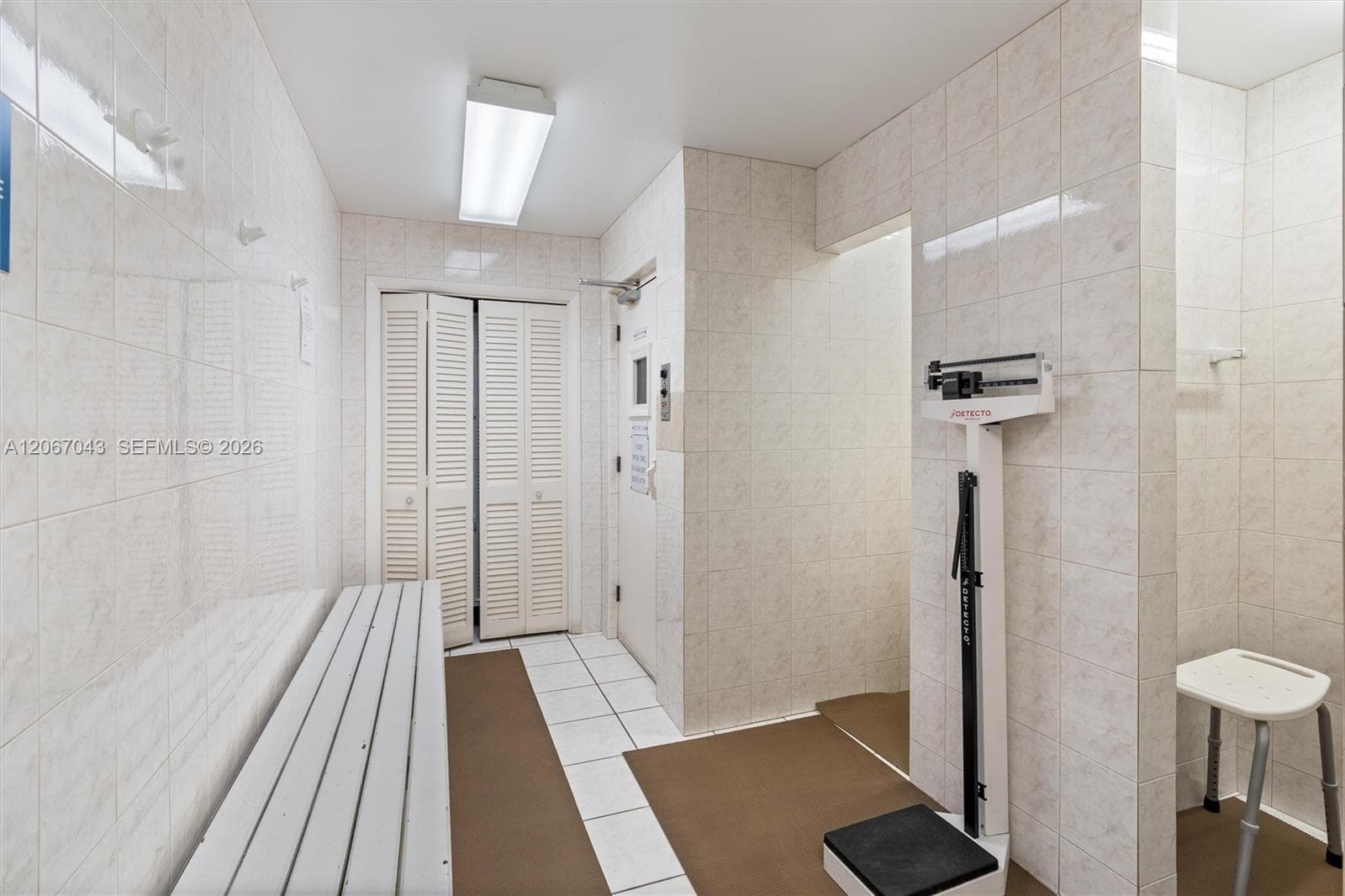 Full-height tiled wall surfacing, built-in louvered closet doors, and overhead fluorescent lighting